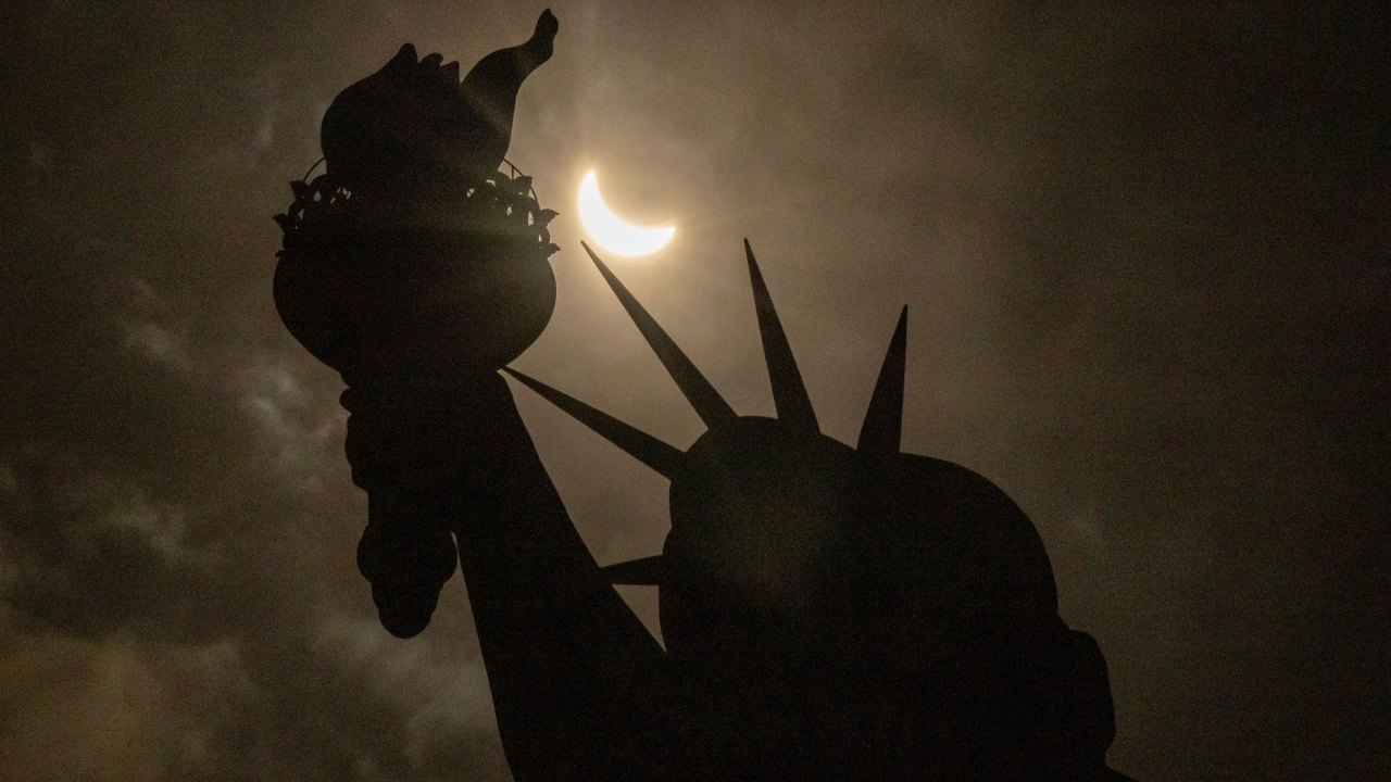 During the solar eclipse the moon partially covers the sun as seen from behind the Statue of Liberty