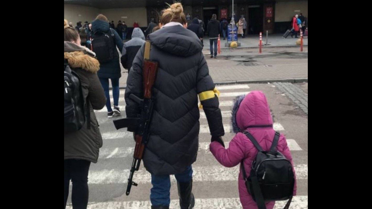 Ukrainian mother with rifle in hand walks with child