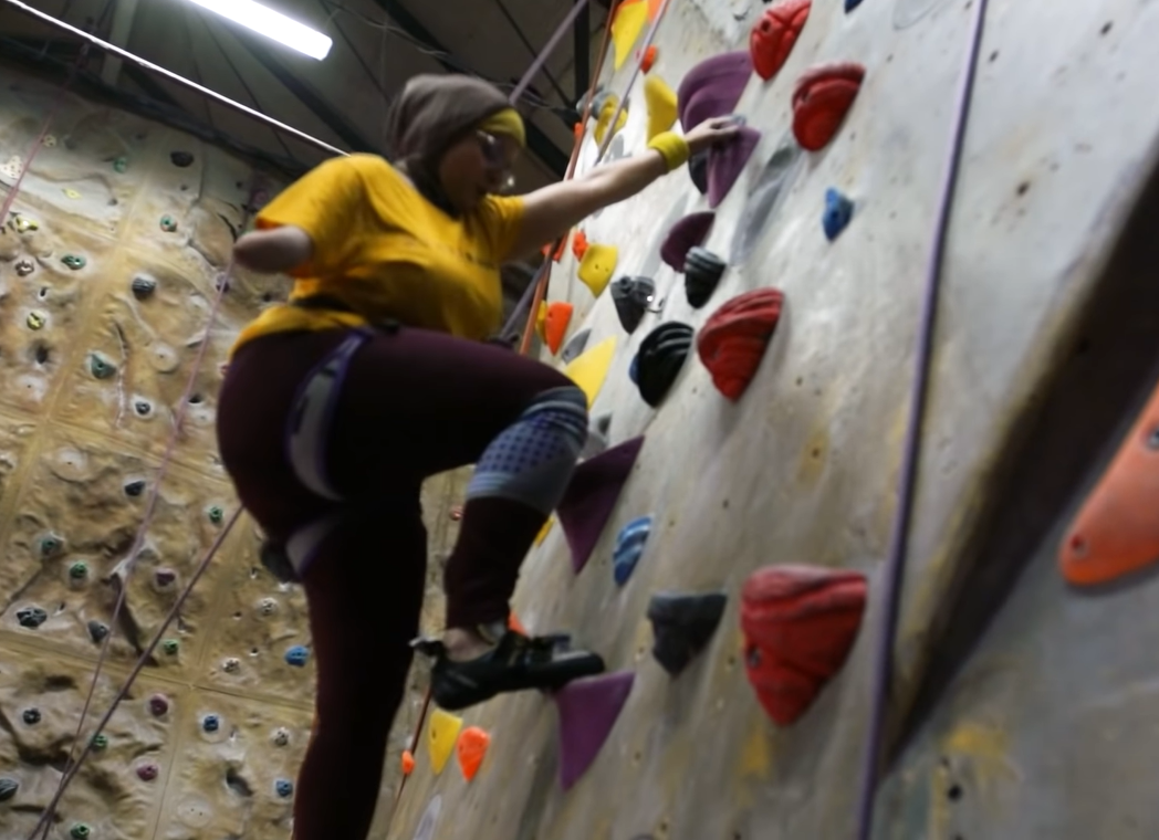 One-handed woman climbs vertical wall