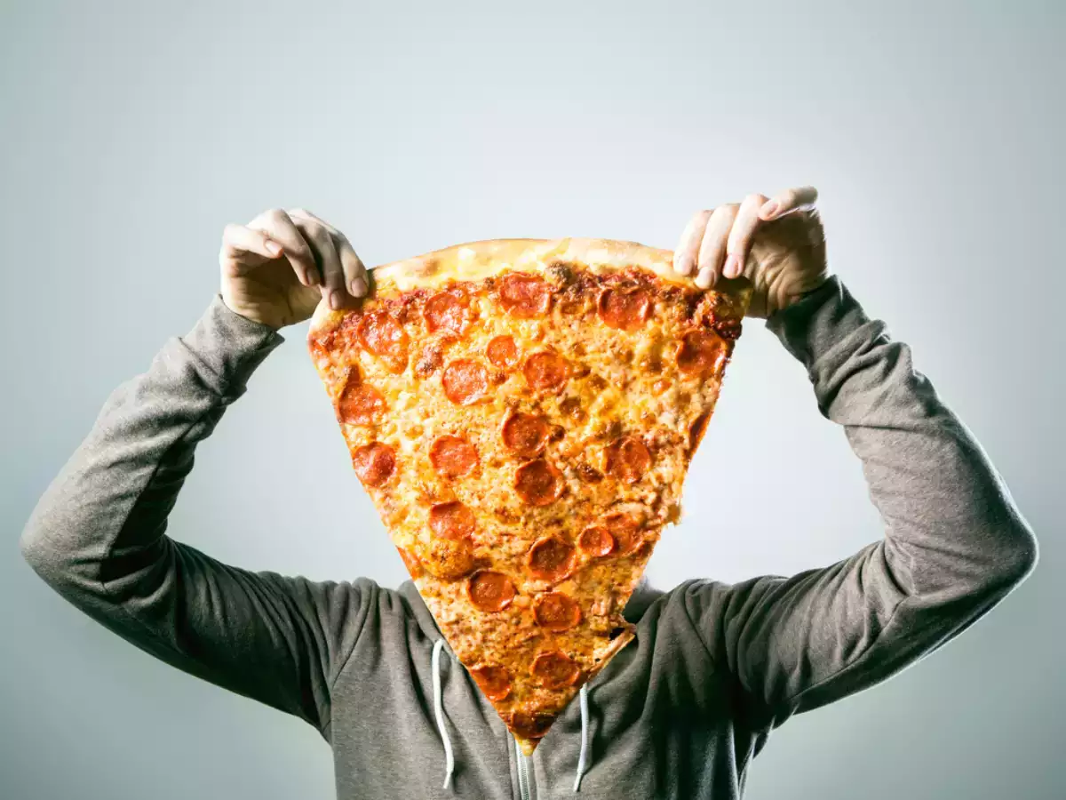 A guy holding a large slice of pepperoni pizza in his hand