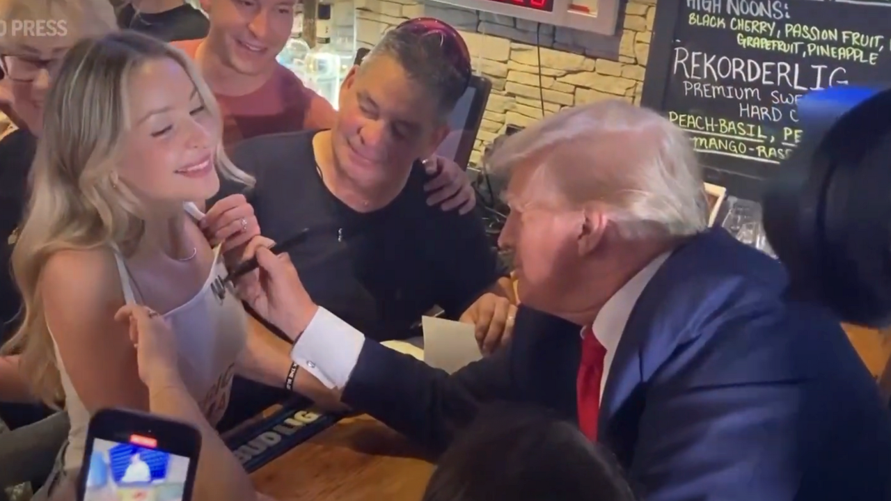 Former US President Donald Trump signs his autograph on a waitress' tank top during a campaign stop at an Iowa pub. | Image courtesy: The Associated Press