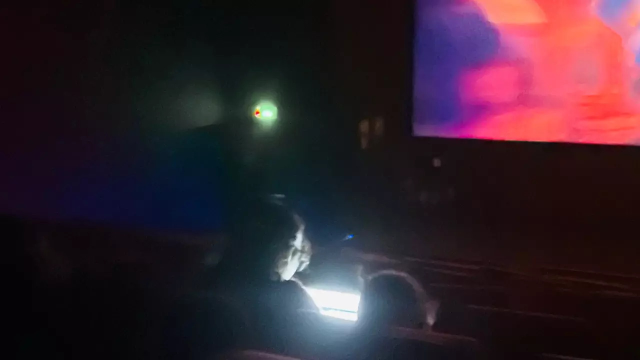 A man works on his laptop during a movie screening in Bengaluru. | Courtesy: @rishfishtish/X