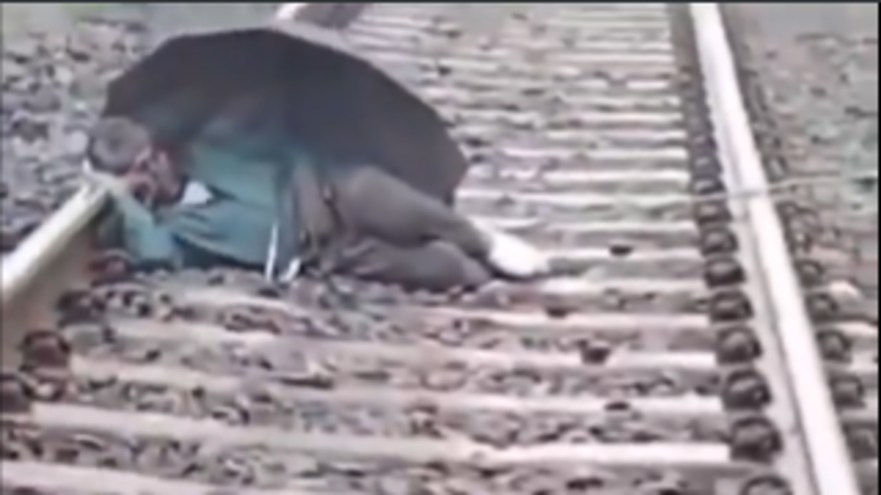 man-holding umbrella sleeps peacefully on railway track even as train approaches | video