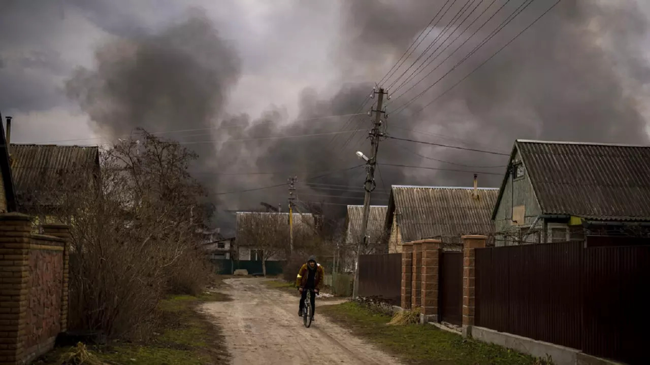 A Ukrainian man rides his bicycle near a factory and a store burning after it had been bombarded in Irpin, on the outskirts of Kyiv