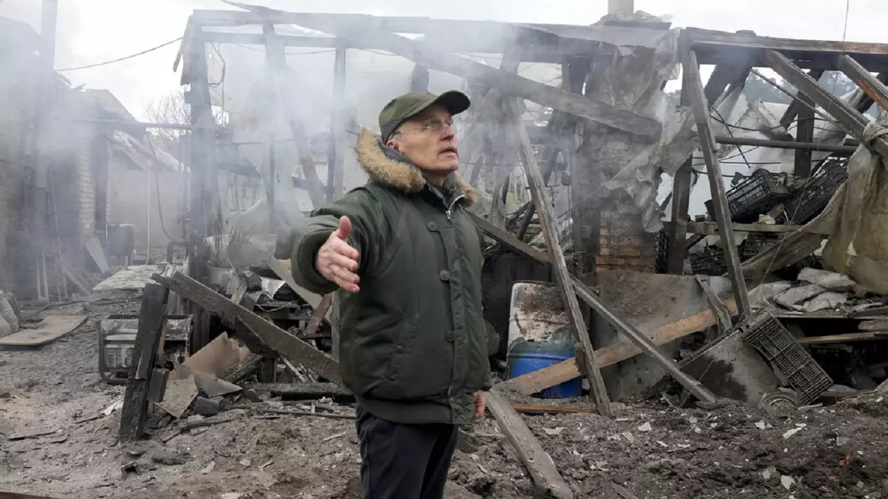 A man opens his arms as he stands near a house destroyed in the Russian artillery shelling, in the village of Horenka close to Kyiv