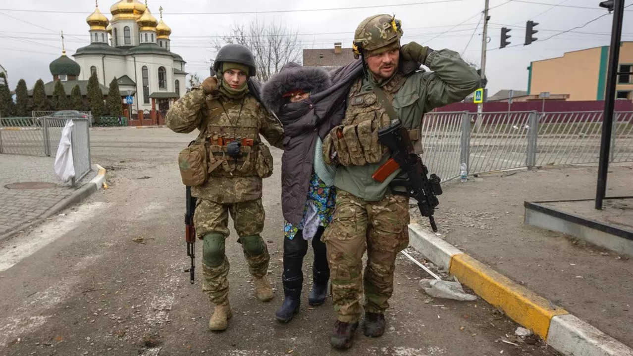 Ukrainian servicemen help an elderly woman in the town of Irpin