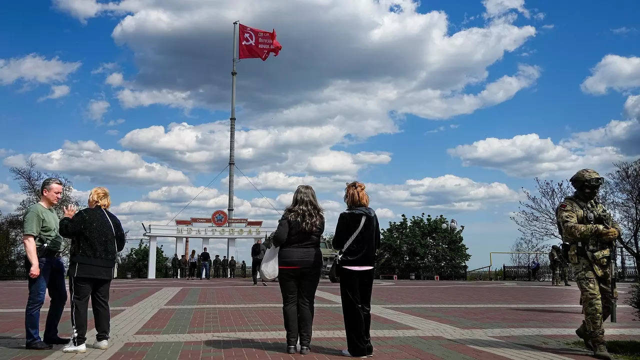 People look as a replica of the Victory banner flutters in the wind over the central square in Melitopol, in territory under Russian military control