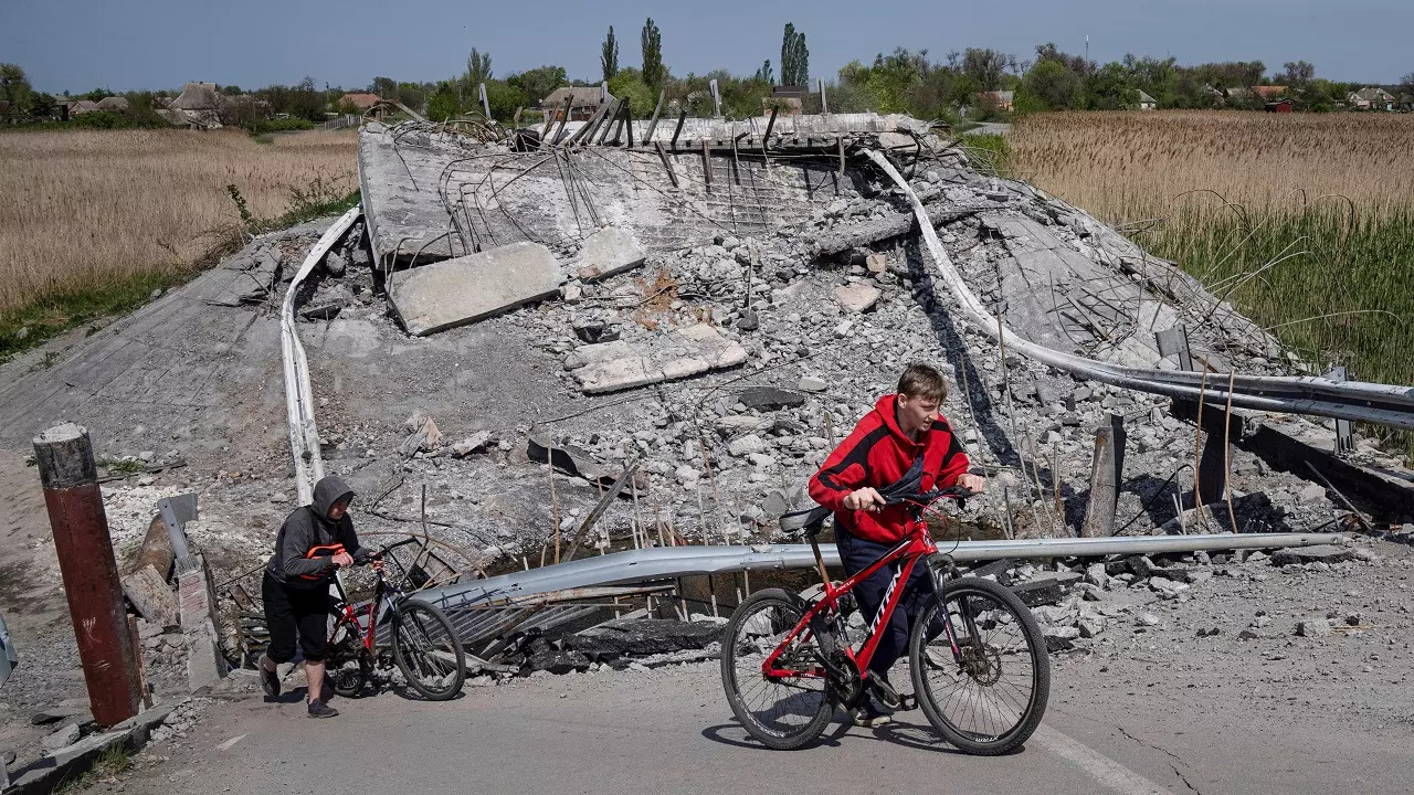 Teenagers on bicycles pass a bridge destroyed by shelling near Orihiv