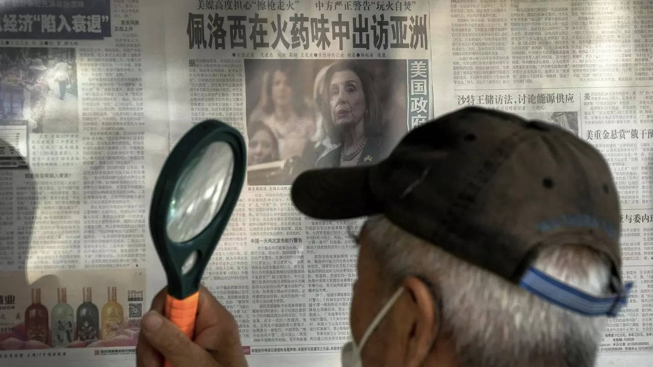 ​A man uses a magnifying glass to read a newspaper headline reporting on US House Speaker Nancy Pelosi's Asia visit, at a stand in Beijing​