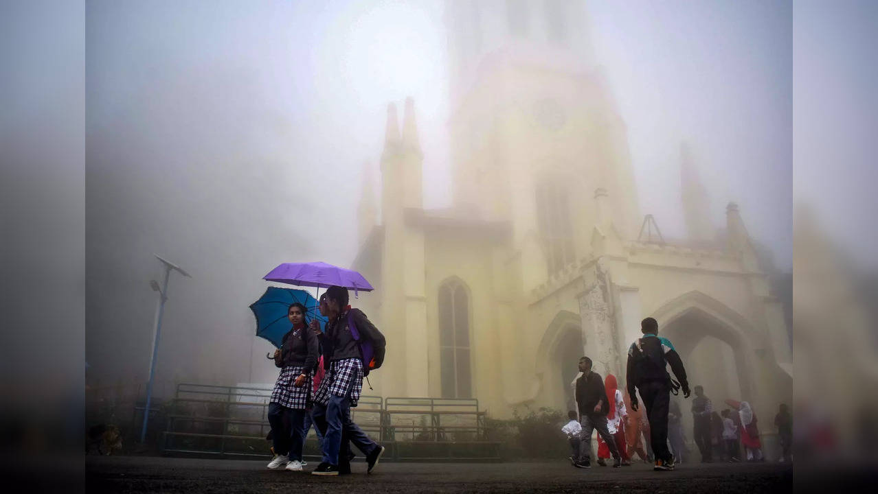 Shimla: People stroll on a misty day in the backdrop of the Christ Church, in Sh...