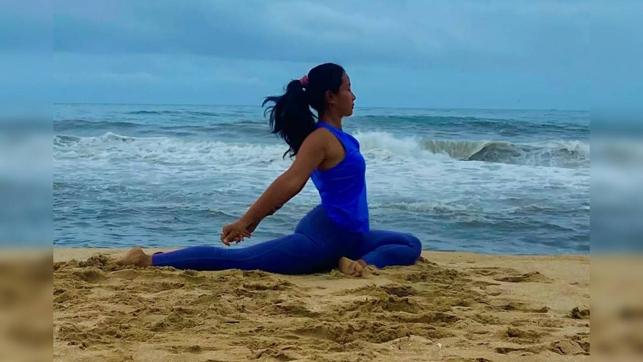 In the picture, Ankita Konwar is seen sitting on the sand with one leg folded from the back and touching her head while the other hand on her foot. (Photo credit: Ankita Konwar/Instagram)