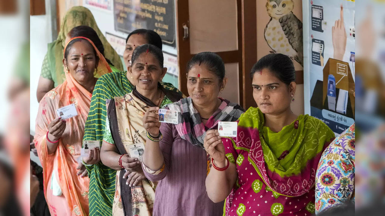 Women show their identity cards as they wait to cast their votes during the first phase of Gujarat state legislature elections in Limbdi