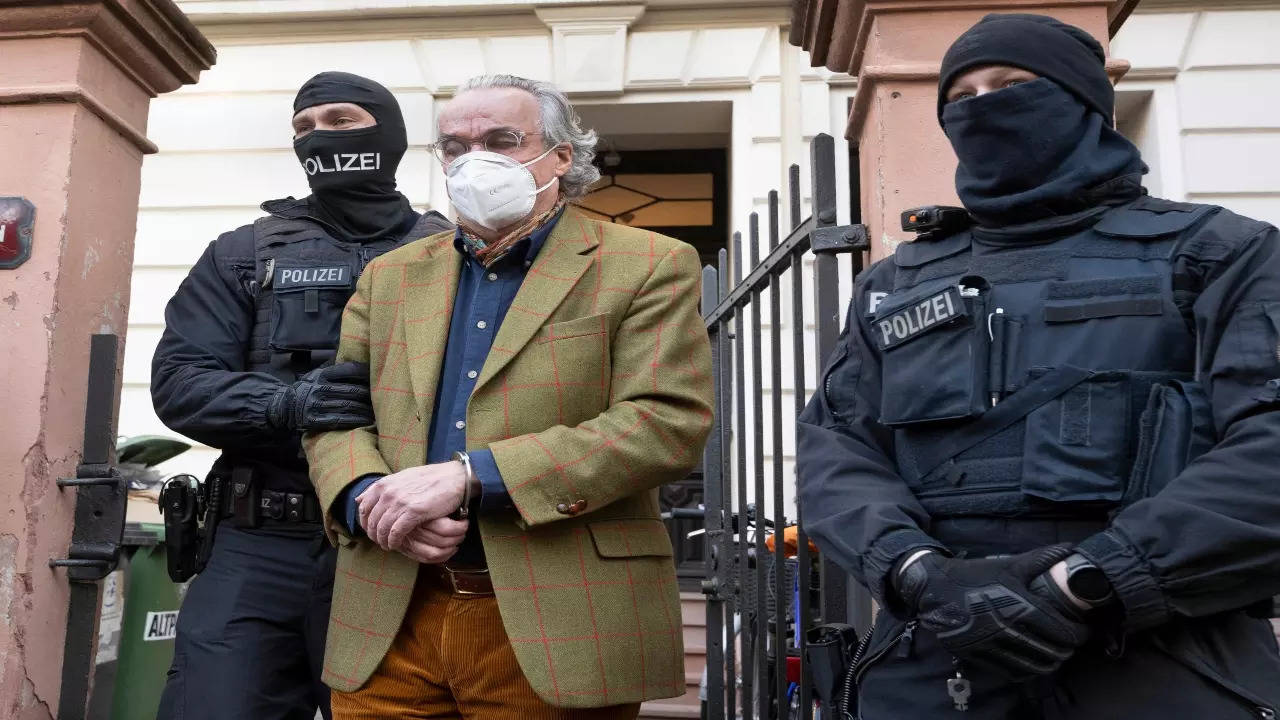 Masked police officers lead Heinrich XIII Prince Reuss, center, to a police vehicle during a raid