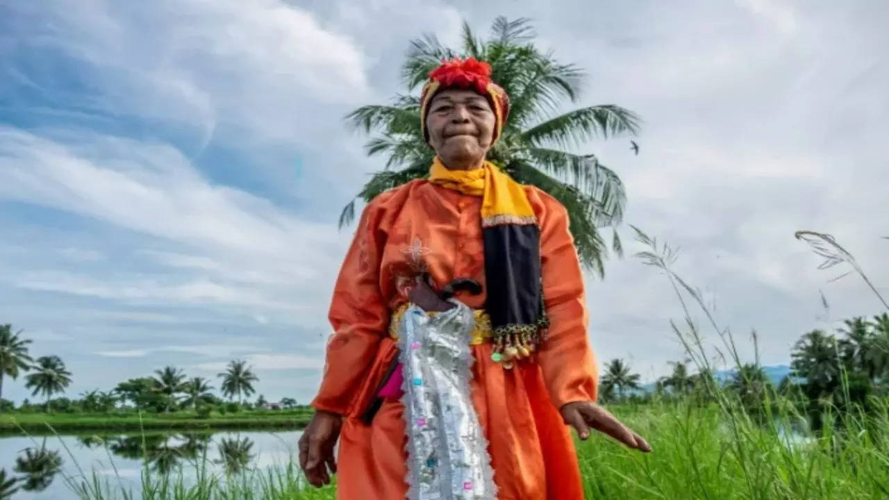 After dawn in a small eastern Indonesia town, a young man holds an ornate umbrella over non-binary p