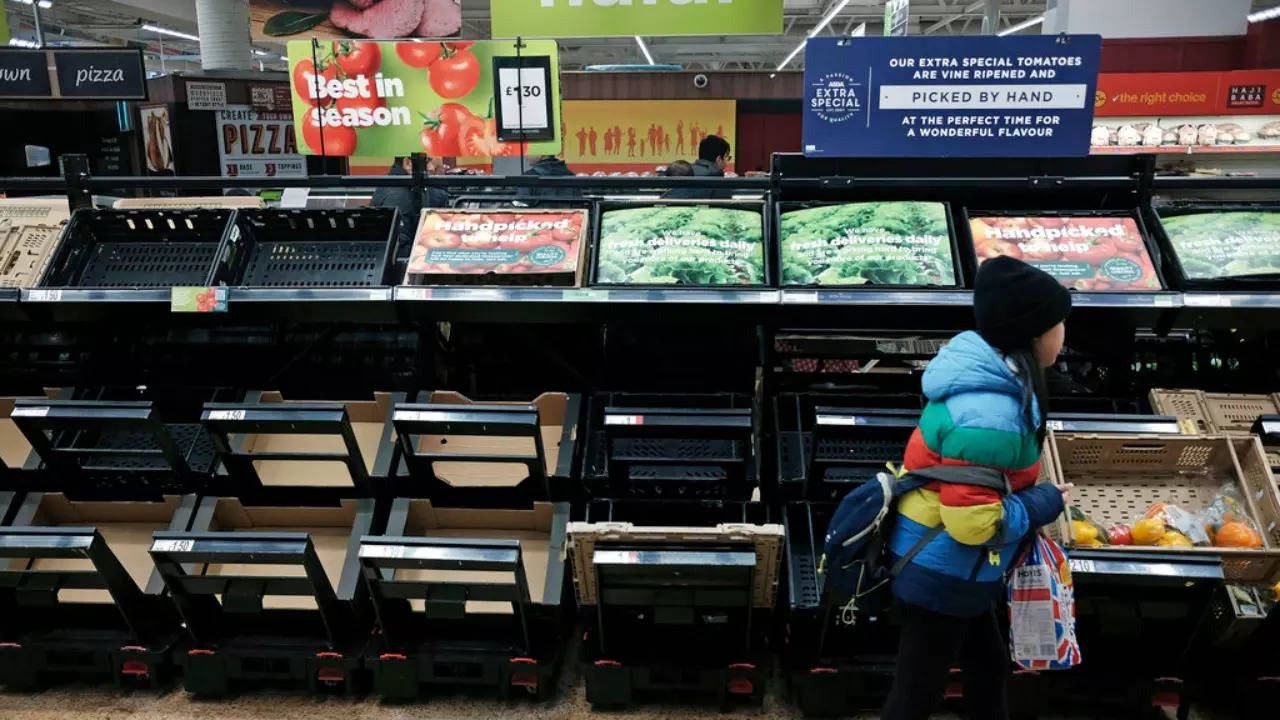 A girl walks by empty fruit and vegetable shelves at an Asda in east London