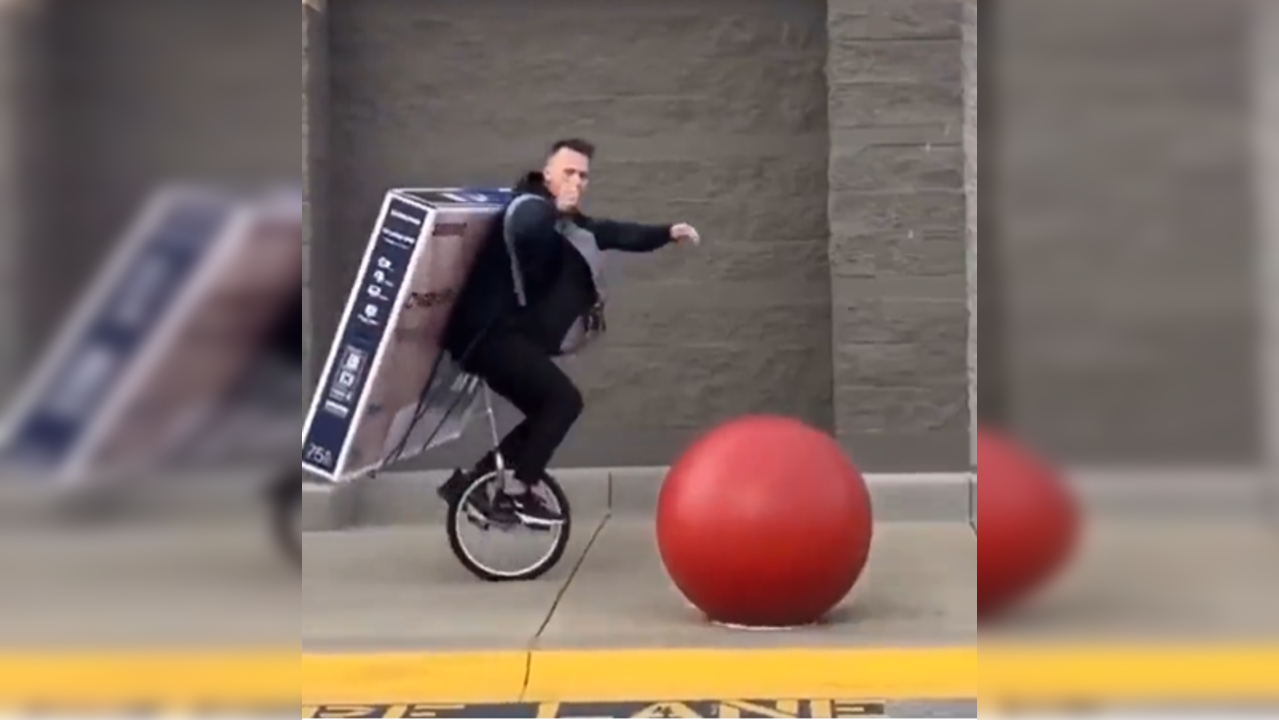 Dude rides unicycle with a 75inch television attached to his back